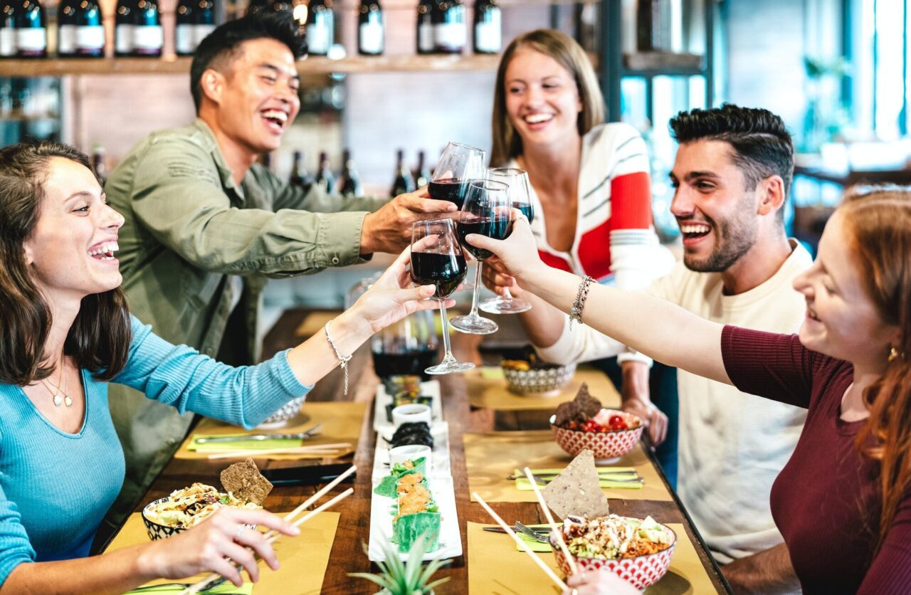 multiracial friends toasting red wine at sushi restaurant